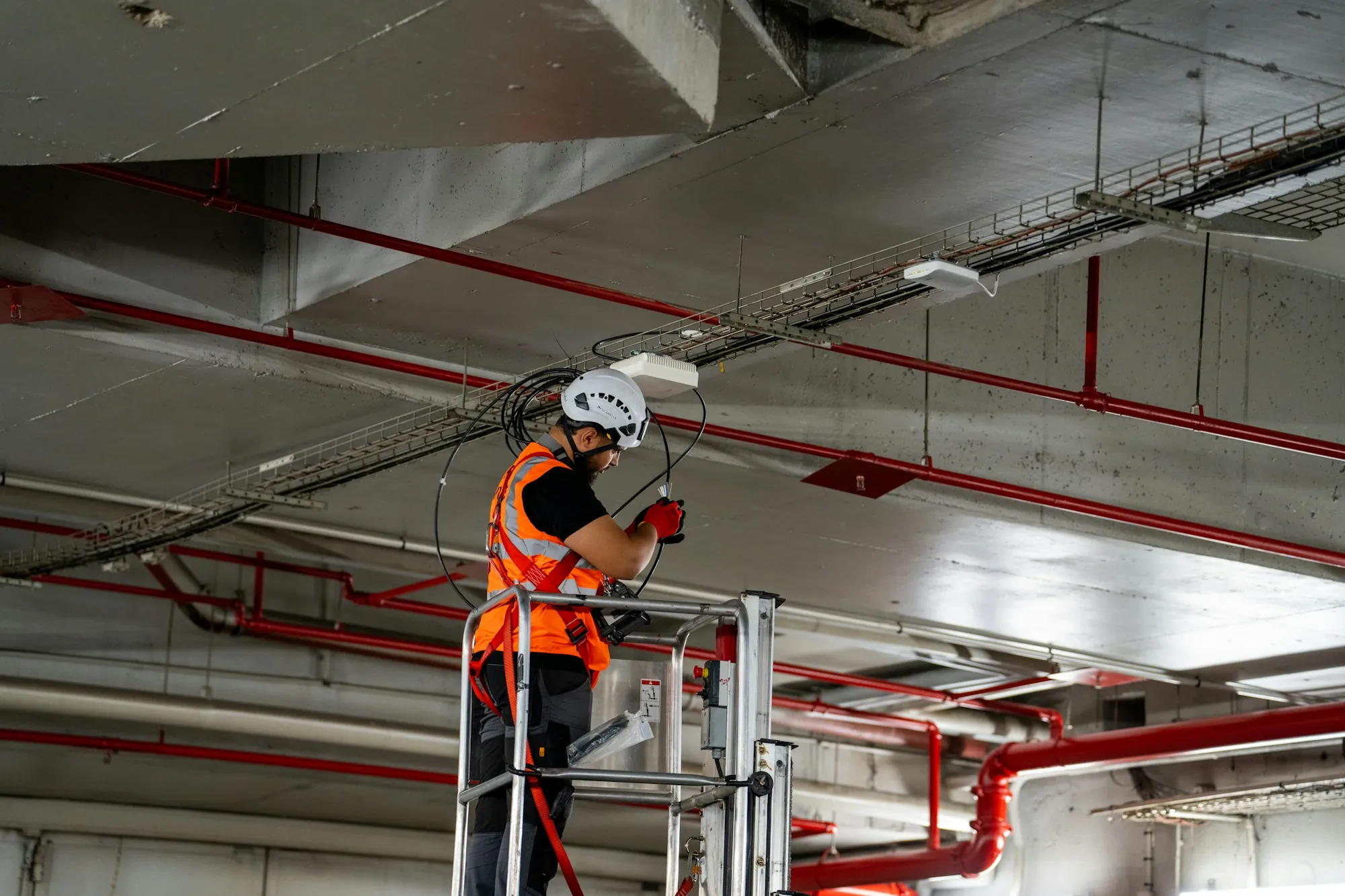Worker in a hard hat and hi-vis vest on a ladder at an open ceiling
